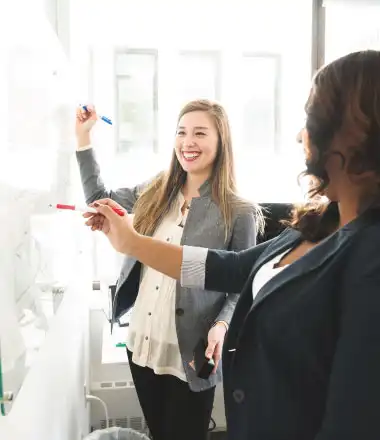 2 businesswomen writing on a white board